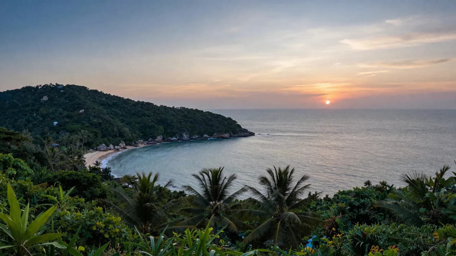 Bay of a tropical island seen from a hillside at dusk, wooded headland and glowing horizon